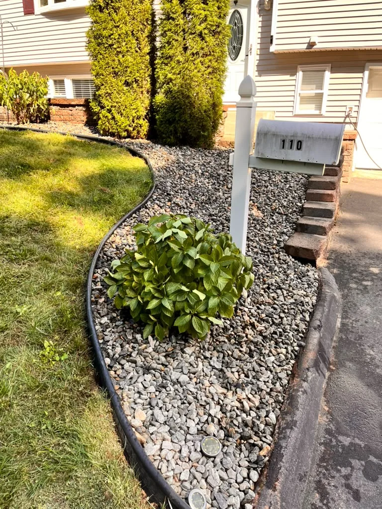 Residential mailbox landscape bed finished with decorative stone and a curved border